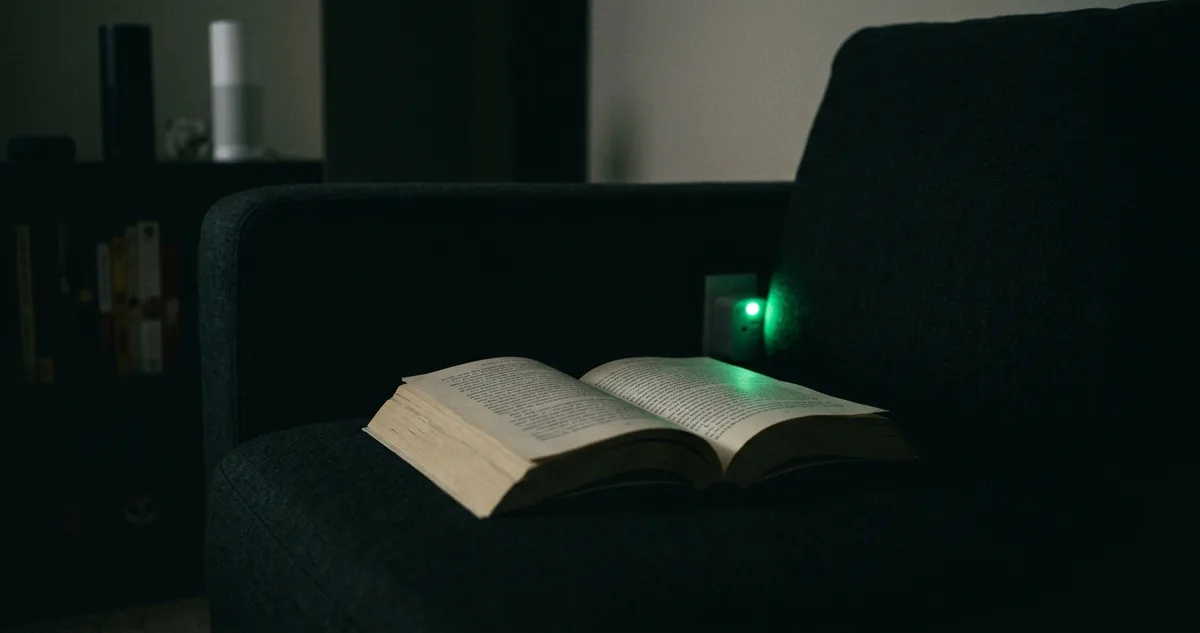 Pessoa lendo no sofá da sala, com um sensor de movimento branco no canto do teto.