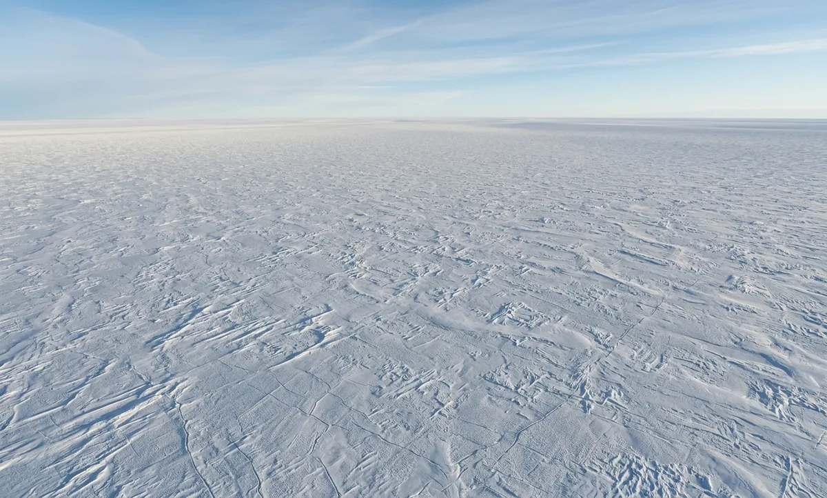 Manto de gelo antártico liso e azulado sob luz polar, sem vegetação nem pessoas, escondendo um lago subglacial