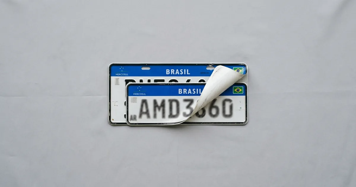Sedã escuro do governo com placa branca de letras pretas parado na porta de uma repartição.
