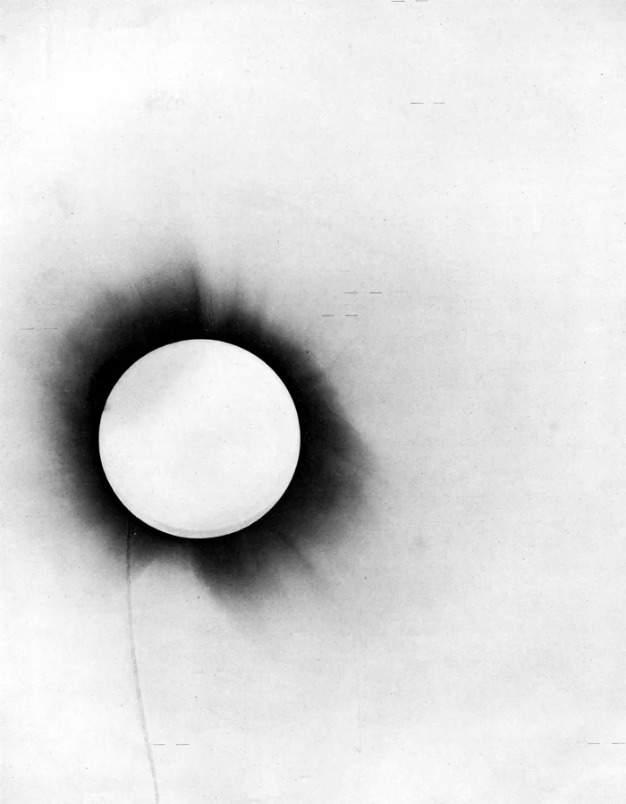 Negativo fotográfico do eclipse total de 29 de maio de 1919, com o disco solar encoberto e traços horizontais marcando as estrelas medidas ao redor da coroa.