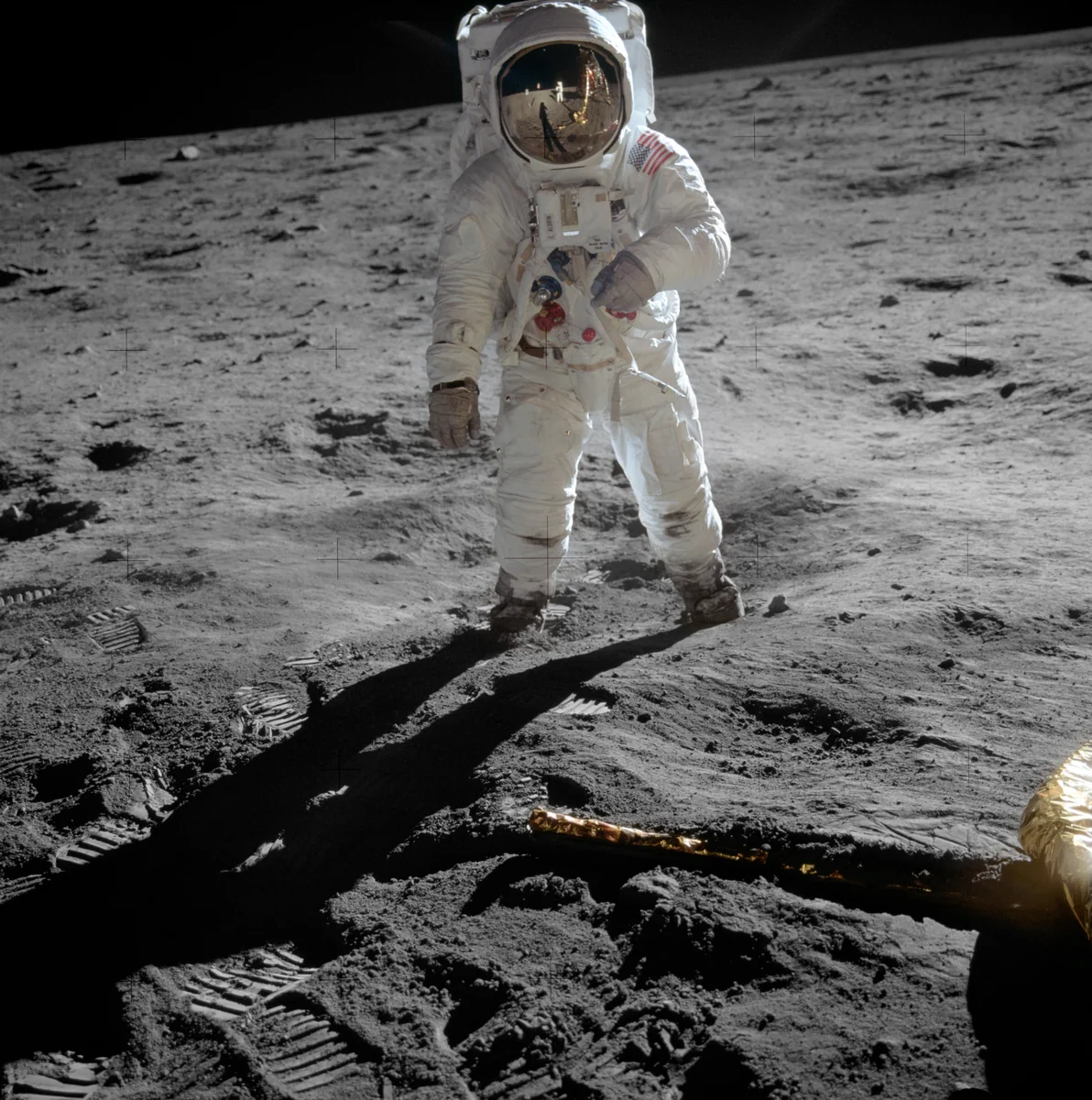 Buzz Aldrin de pé na superfície lunar em 1969, com Neil Armstrong e o módulo lunar refletidos no visor dourado do capacete.