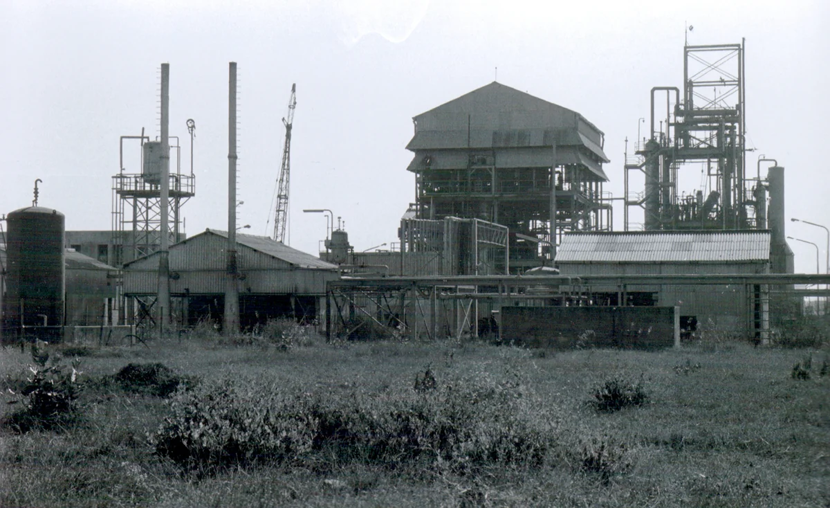 Vista externa da fábrica de pesticida da Union Carbide em Bhopal, Índia, com a tubulação aérea e o concreto manchado, fotografada por Martin Stott para o Bhopal Medical Appeal.