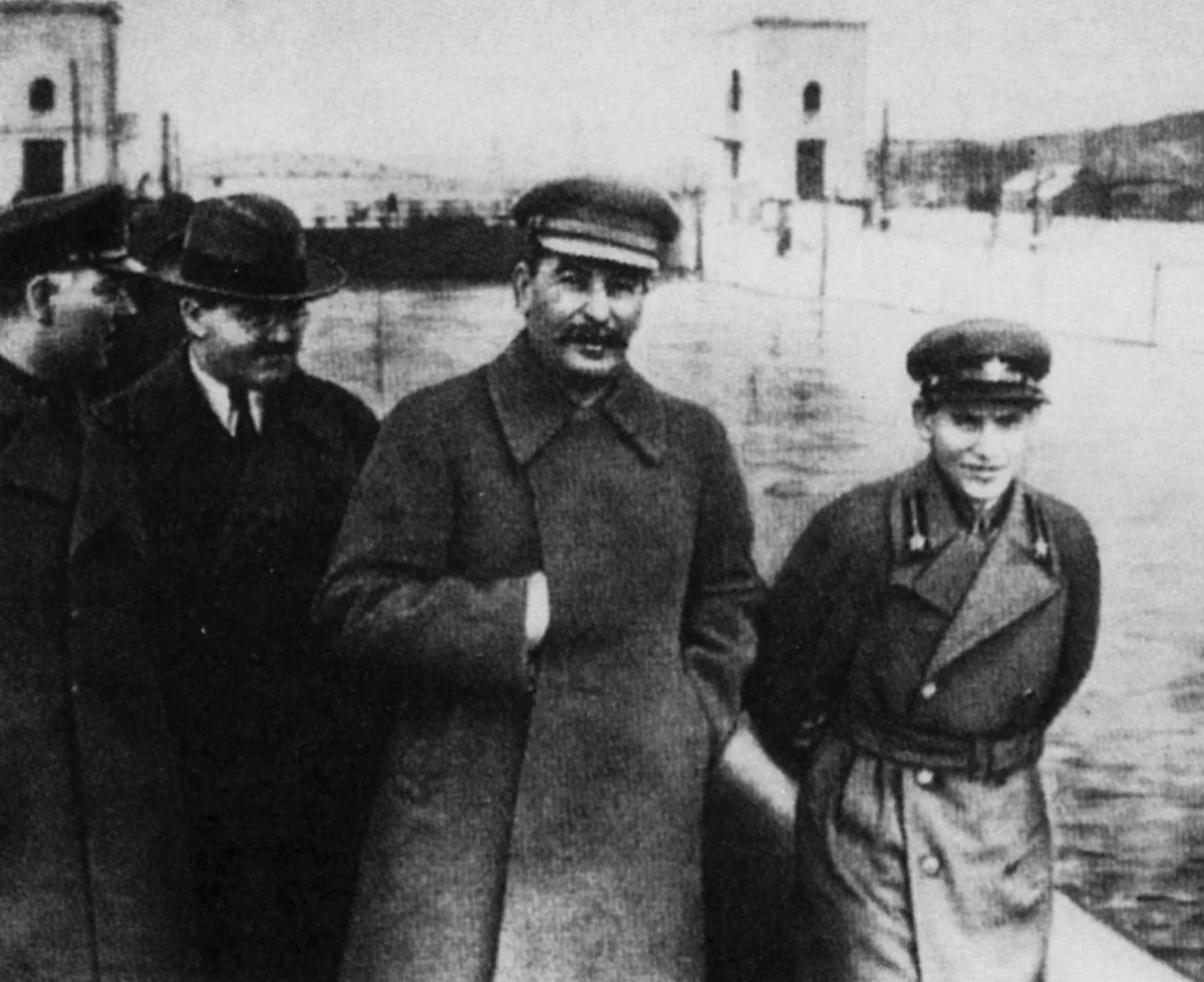 Stálin, Molotov, Vorochilov e Iejov encostados na mureta de concreto do canal Moscou-Volga, com a água ao fundo.