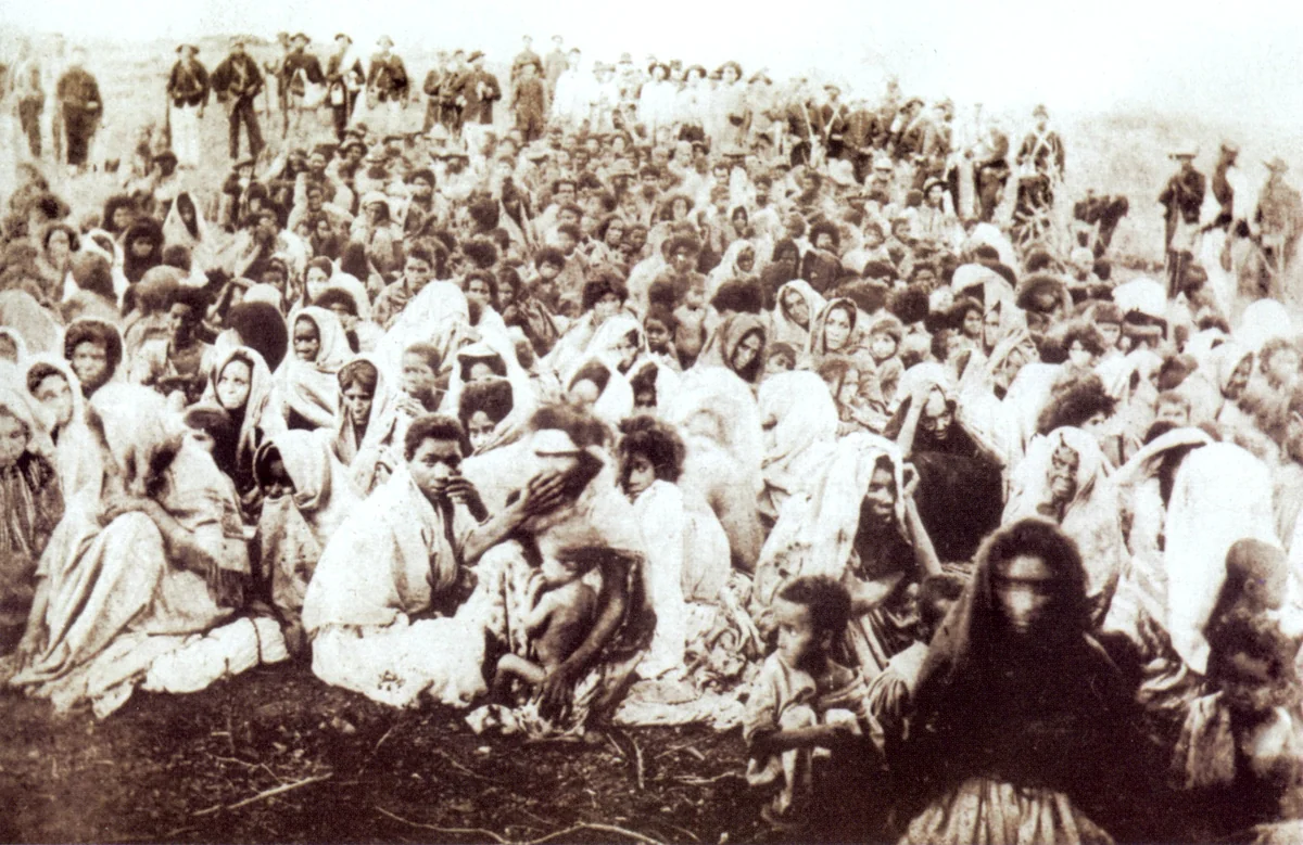 Mulheres, crianças e velhos rendidos em Canudos sentados no chão do acampamento do Exército, sertão da Bahia, 1897.