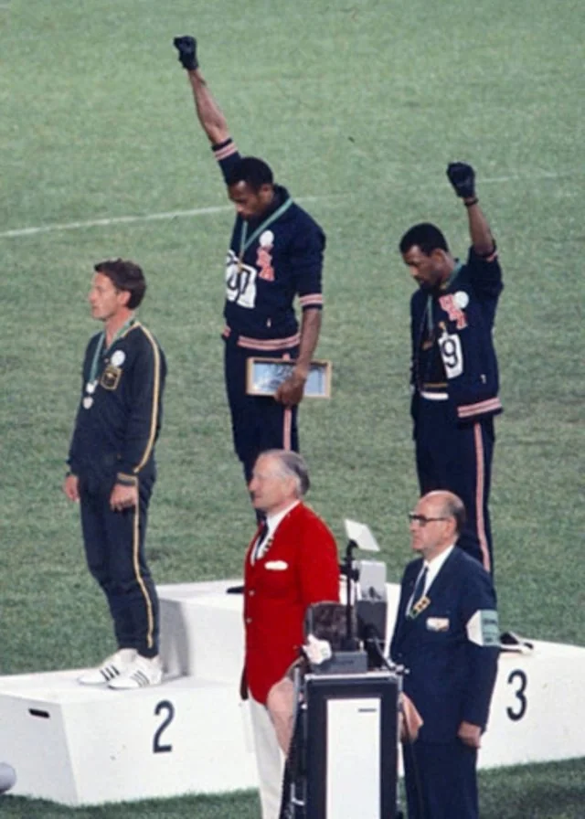 Tommie Smith e John Carlos erguem o punho enluvado no pódio dos 200 metros, com Peter Norman à frente, na Cidade do México, em 1968.