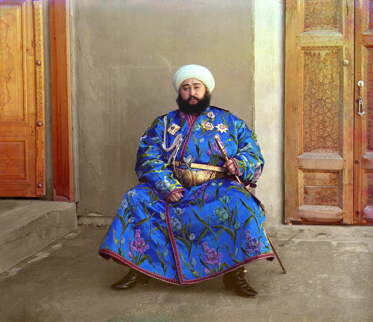 Said Mir Mohammed Alim Khan, emir de Bukhara, de pé com turbante branco, manto de seda azul estampado de flores e sabre na cintura, em foto colorida de Sergei Prokudin-Gorsky, 1911.