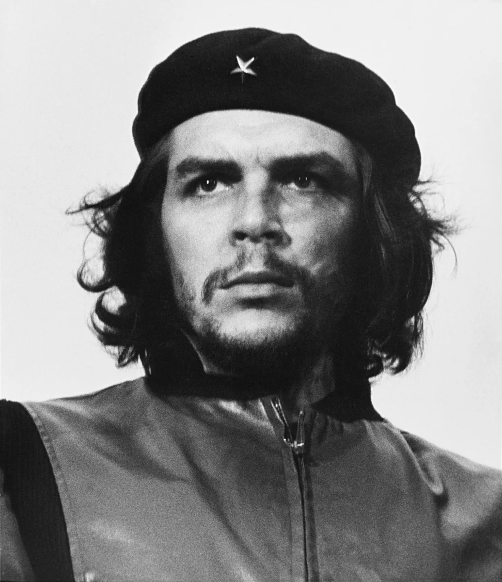 Ernesto Che Guevara de boina escura com estrela, cabelo comprido e jaqueta fechada até o pescoço, olhando para o alto, na foto Guerrillero Heroico de Alberto Korda, 1960.
