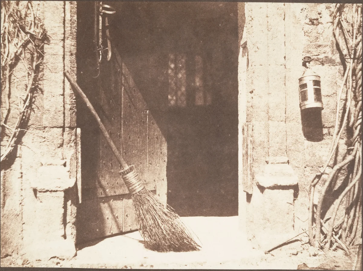 Calótipo de William Henry Fox Talbot, 1844: porta de estábulo entreaberta em Lacock Abbey, com vassoura e lanterna