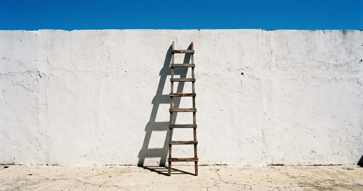 Muro caiado sob sol de meio-dia, com a escada externa projetando sombra curta e de borda dura na parede.