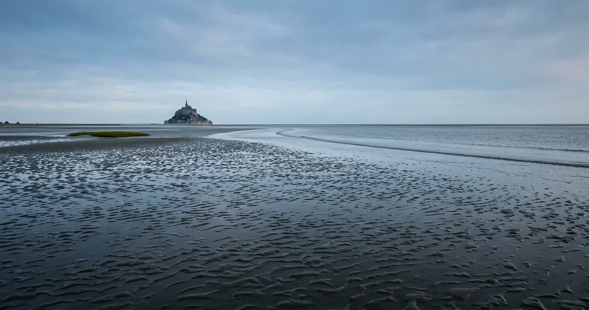 O Monte Saint-Michel cercado pela maré cheia, com a abadia no topo do rochedo e a baía alagada em volta.