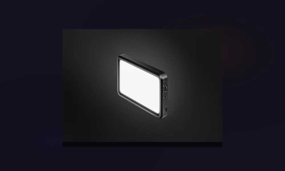 Painel de LED pequeno num minitripé iluminando o rosto numa escrivaninha de hotel